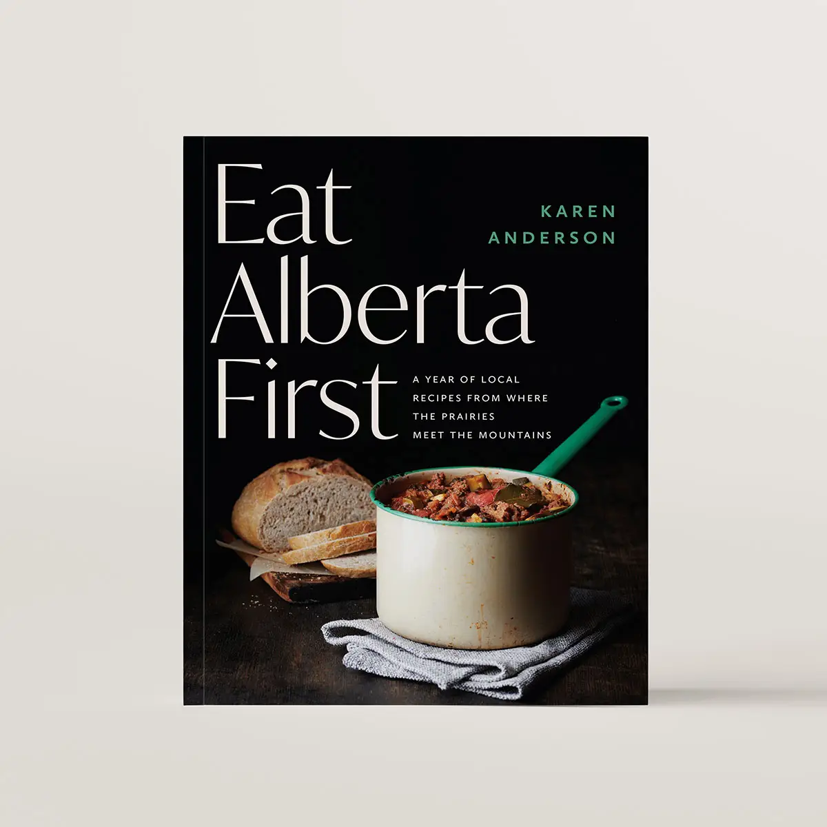 Book cover of Eat Alberta First. The cover features a dark photo of a stew in a pot with a sourdough loaf beside it. 